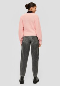 Un pull à côtes rose clair avec des épaules basses, associé à un jean gris foncé taille haute et des bottines noires, vu de dos.