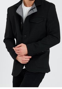 Czarna kurtka z teksturowanej tkaniny, z szarym kołnierzem w paski, przednią kieszenią naszywaną i zapięciem na guziki. Krój slim fit.