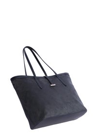 Gran bolsa tote negra con dobles asas y un pequeño acento plateado en la parte superior, mostrado contra un fondo blanco.