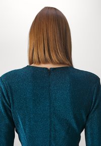 Teal, glittrig klänning med rund halsringning och en dragkedjedetalj på baksidan, med en mjuk och len tygkänsla.