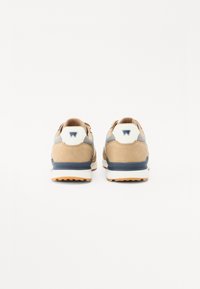 Pruunist nahast ja võrgust sneakers'id, millel on valge ja hall aktsent, ning tumesinine talla ja logo detail kanna peal. Nähtavad tekstuuriga kangad.