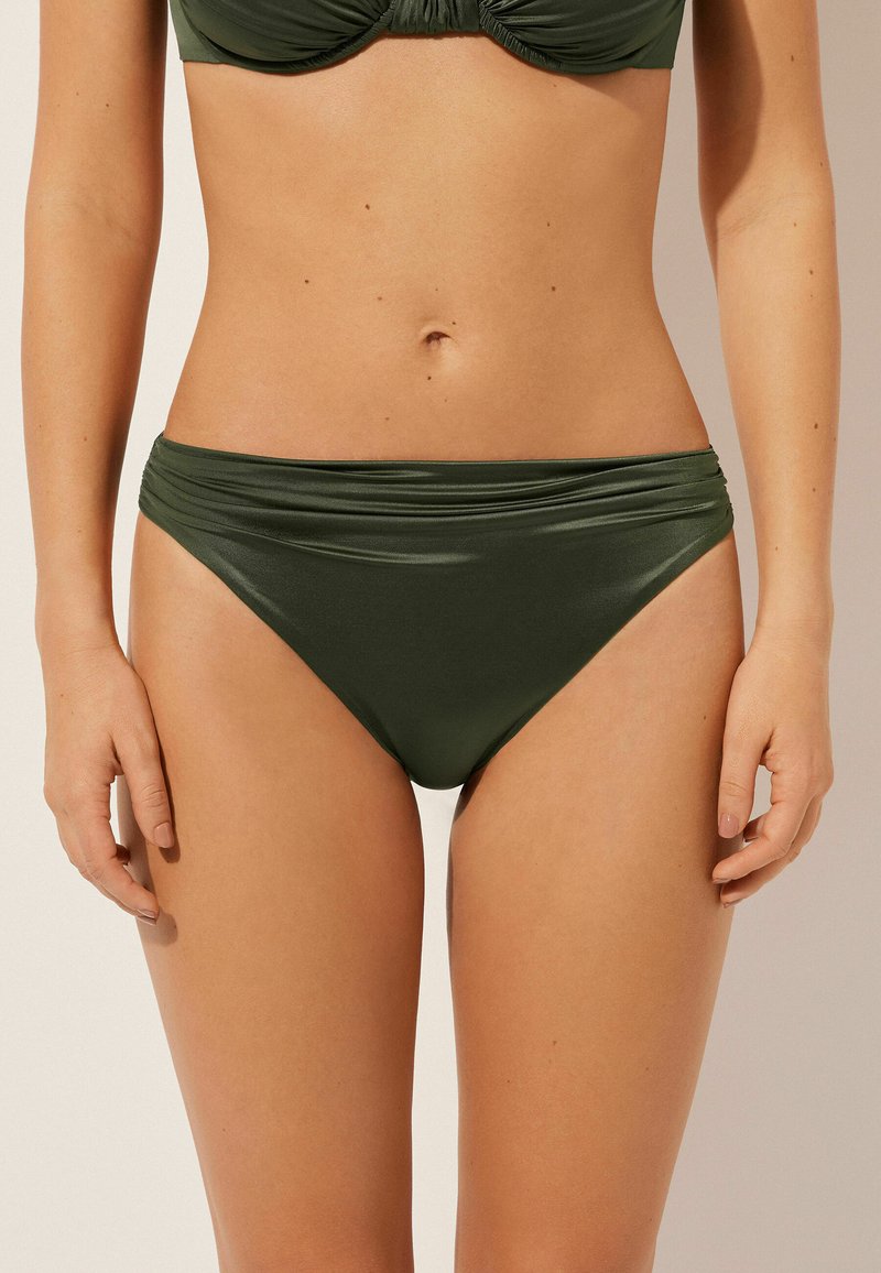 Zelené bikiny s hladkým, elastickým materiálem. Mají široký pás s nařasenými detaily. Středně vysoký a těsně přiléhající střih.