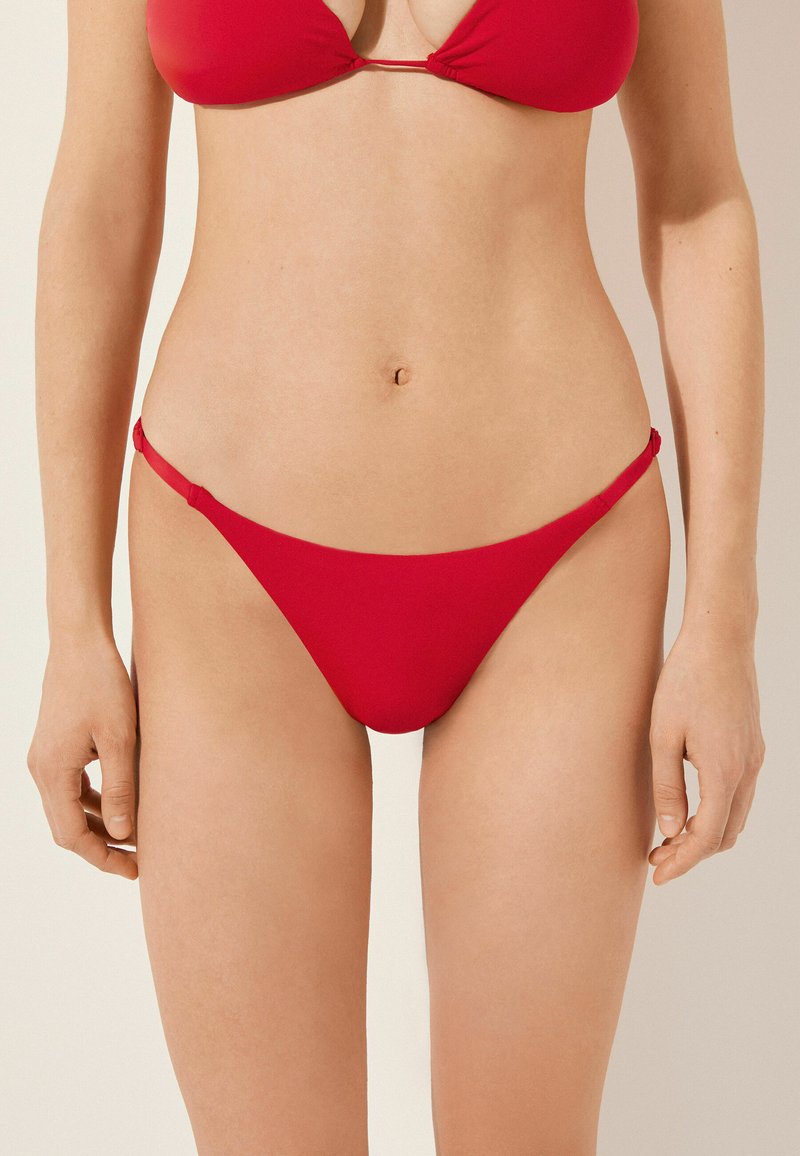 Röd bikini-set med triangeltopp och minimalt täckande botten med tunna sidoremmar. Slät tyg utan synliga mönster.
