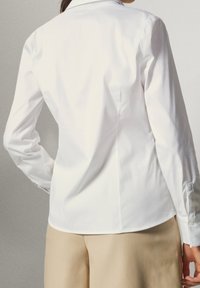 Witte longsleeve shirt met een klassiek colletje, getailleerd ontwerp, gladde textuur en met knopen bij de manchetten, gecombineerd met beige broeken.