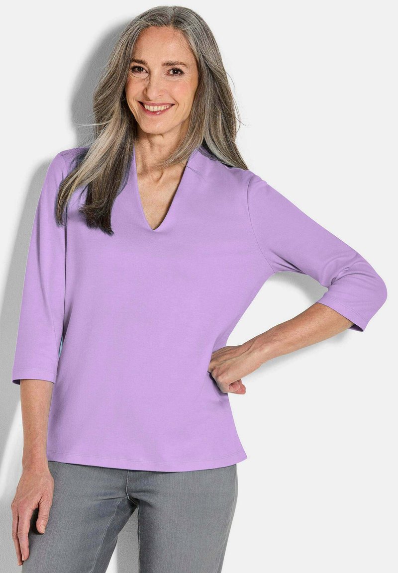 Lavender top met driekwart mouwen en een V-halsontwerp, van zachte stof en een relaxte pasvorm, gecombineerd met grijze broek.
