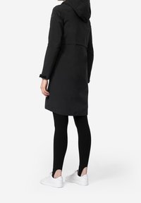 Manteau noir imperméable avec capuche, longueur mi-cuisse, doté de manches douces et d'un design élégant. Assorti à des leggings noirs et des baskets blanches.