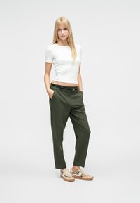 Weißes, kurzes Crop-Top mit kurzen Ärmeln, olivgrüne, tapered Hosen und gemusterte Turnschuhe. Minimalistisches Design mit lockerem Schnitt und gedämpften Farben.