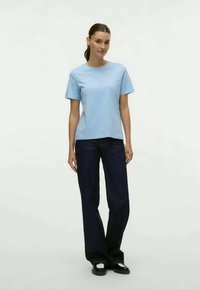 Šviesiai mėlynas medvilninis marškinėliai su trumpomis rankovėmis ir apvaliu iškirpimu, derinami su plačiomis tamsiai mėlynomis kelnėmis ir plokščiais juodais batais.