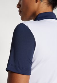 Πόλο μπλούζα κοντομάνικη με ναυτικό μπλε γιακά και μανίκια, λευκό σώμα, λεία υφή και ραφές στο τελείωμα.