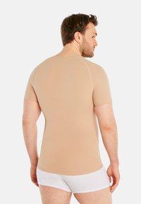 Beige short-sleeve fitted shirt made of smooth fabric, with a crew neckline and contrast stitching, worn with white shorts.