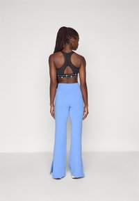 Črn športni modrček z mrežastim izrezom na hrbtu, v kombinaciji s svetlo modrimi flare hlačami, ki imajo stranske reze. Gladek material z sproščenim krojem.