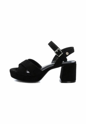 Sandalias de ante negro con tacón cuadrado que presentan un diseño de tiras cruzadas, correa de tobillo ajustable con hebilla y punta redondeada.