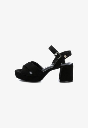 Sandalias de ante negro con tacón cuadrado que presentan un diseño de tiras cruzadas, correa de tobillo ajustable con hebilla y punta redondeada.