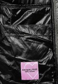 Svart, glänsande innerv Beige med en rosa lapp som läser "ANIMALFREE 100% VEGAN." Har en slät textur och en sydd rektangulär detalj.