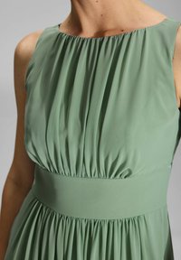 Robe verte sans manches avec un corsage froncé et une taille élastique. Texture lisse, design fluide et éclat subtil.