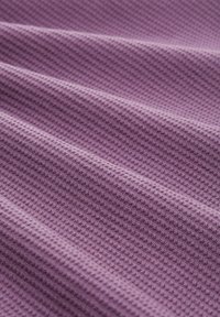 Tessuto tessuto in lavanda, con un motivo testurizzato simile a un waffle. Il tessuto presenta pieghe morbide, evidenziando la sua natura pliabile.
