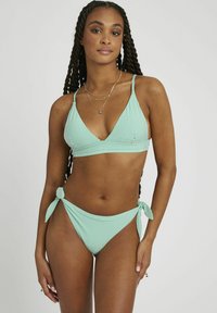 Ensemble bikini rayé en vert et blanc. Le haut présente un design triangulaire avec des fines bretelles ; le bas a des accents de nouage au niveau des hanches et des jambes à taille haute.