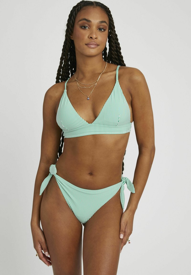 Ensemble bikini rayé en vert et blanc. Le haut présente un design triangulaire avec des fines bretelles ; le bas a des accents de nouage au niveau des hanches et des jambes à taille haute.