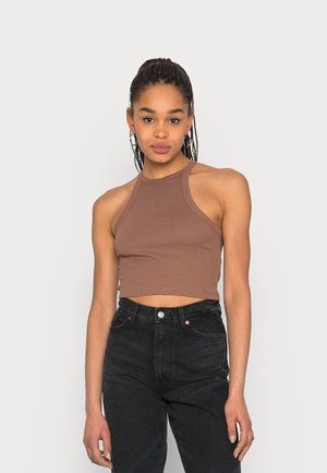 Top cropped halter em tom castanho com design ajustado, combinado com jeans pretos de cintura alta. Apresenta um estilo sem mangas e uma gola minimalista.