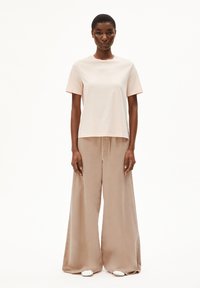 Lichtroze katoenen T-shirt met korte mouwen en een ronde halslijn, gecombineerd met beige broek met wijde pijpen en witte schoenen.