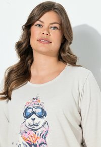 Helles beige Langarmhemd mit einem Grafikmotiv eines Eisbären in Sonnenbrille und buntem Schal, mit filigranen Details im Design und in der Textur.