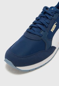 Navy blue athletic shoe featuring a textured fabric upper, padded collar, white accents, and light blue rubber sole with a stitched design.