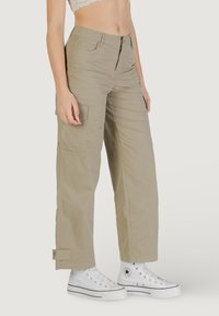 Pantalones cargo color caqui con cierre de cremallera y botón, con bolsillos laterales y puños. El material es ligero y suave. Combinados con zapatillas blancas.