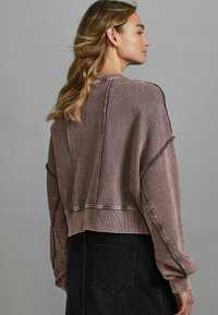 Felpa mauve scolorita con una vestibilità ampia, caratterizzata da dettagli a coste e cuciture consumate. Abbinata a una gonna nera, che mette in mostra uno stile casual.