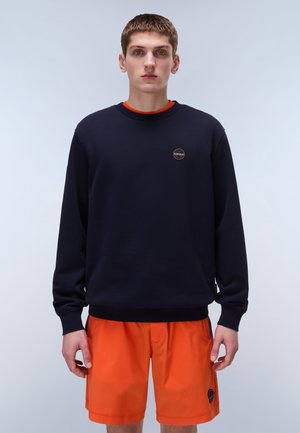 Navy sweatshirt with round logo, crew neckline, long sleeves, and ribbed cuffs, paired with bright orange shorts. Smooth fabric texture.