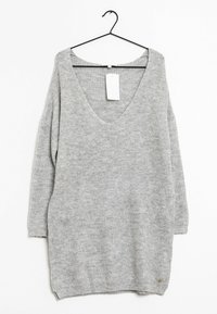 Maglione grigio chiaro, a maniche lunghe, lavorato a maglia, con scollatura a V, appeso a un appendiabiti nero su sfondo bianco.
