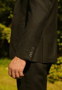 Czarna marynarka w jodełkę o dopasowanym kroju, z czterema błyszczącymi guzikami na mankiecie i gładką fakturą. Szykowny design z ostrymi liniami.