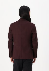 Burgundy kavaj med skräddarsydd design, med slagkrage, enkel slits och knappdekorationer på ärmarna. Slät tissu.