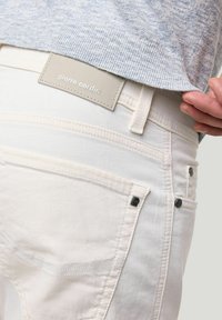 Witte denim jeans met een textuurafwerking, voorzien van een zichtbare label, subtiele stiksels en zwarte hardware-accenten.