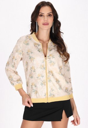 Beige bomberjakke med et blomsterdesign i gul og grøn, struktureret stof, ribbede manchetter og halsudskæring i gul samt lynlås-lukning.