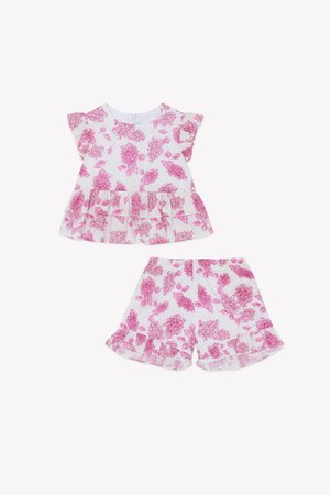 White outfit with pink floral pattern, featuring a ruffled short-sleeve top and matching shorts, both with a layered ruffle hem.