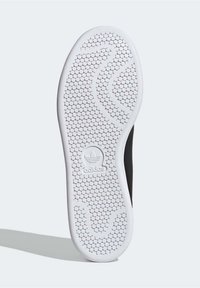 Weiße Gummisohle mit sechseckigem Muster und wellenförmigem Design, in der Mitte mit einem Adidas-Logo. Sichtbare schwarze Seitendetails.