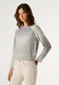 Suéter de mezcla de lana gris claro con un cuello de canalé rosa y mangas raglán grises; textura suave y diseño ajustado. Combinado con jeans de color claro.
