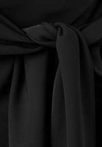 Gros plan d'une ceinture en tissu noire nouée d'un nœud simple sur un vêtement noir texturé.