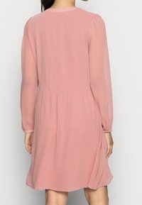 Roze, lange mouwen jurk met een ronde halslijn, geplooide details bij de schouders en een vloeiende rok die boven de knie valt. Lichtgewicht stof.