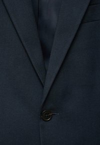 Granatowa marynarka z klapami typu notch i pojedynczym czarnym guzikiem zapiętym z przodu.