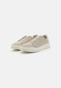 Beige Wildlederschuhe mit niedrigem Schnitt, elastischen Schnürsenkeln und einer weißen Gummisohle. Sie zeichnen sich durch eine glatte Textur und eine minimalistische Ästhetik aus.