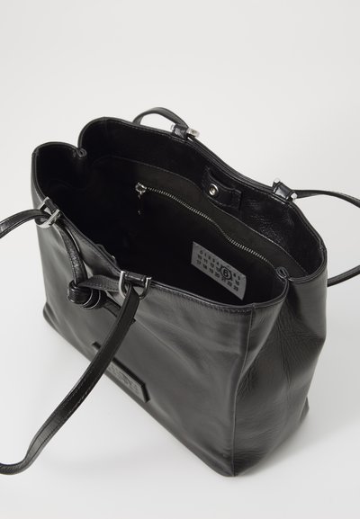 Black leather tote bag with two straps, open top revealing interior zippered pocket and white label inside.