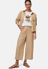 Beige vide bukser parret med en hvid grafisk t-shirt med et design af en brun støvle. Modellen har brune strappy sandaler på.