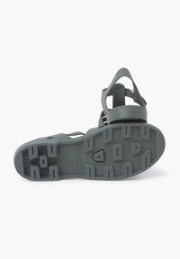 Gray rubber sandal with a ridged sole, adjustable strap, and multiple cutouts for ventilation. Flat design for casual wear.
