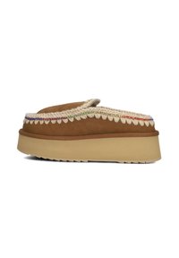 Pantofole scivolose in suede marrone con rivestimento in pelo sintetico crema, dettagli decorativi di cucitura intrecciata e suola in gomma testurizzata.