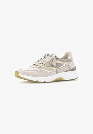 Beige sneaker met witte zool, mesh panelen, rits en veters, en een gumkleurige, gestructureerde buitenzool, zijaanzicht op een witte achtergrond.