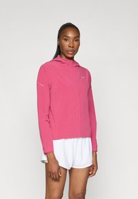 Veste légère rose avec capuche et manches longues, dotée d'accents réfléchissants sur les épaules et d'une fermeture éclair devant.