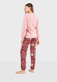 Haut rose clair à manches longues associé à un pantalon de survêtement bordeaux à motifs avec des designs floraux et graphiques. Tissu doux, coupe décontractée.