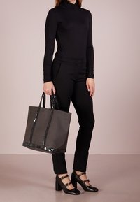 Grijze draagtasje met glanzende zwarte accenten, stevige handvatten en een rechthoekige vorm, gecombineerd met een zwarte aansluitende top en broek.