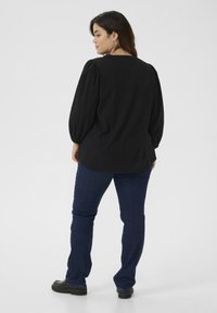 Schwarze, gerippte Bluse mit schulterlangen Puffärmeln, rundem Ausschnitt und fließendem Schnitt, kombiniert mit dunkelblauen Jeans und schwarzen Plateauschuhen.